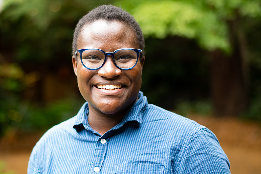 A woman with close-cropped hair and blue glasses looks directly into the camera, smiling.; Learn More