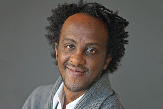 A man in a gray cardigan and white shirt smiles into the camera, behind him a gray background.; Read More in the&nbsp;New York Times