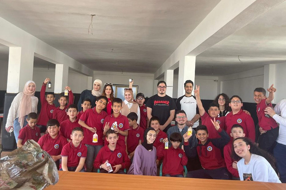 Group of elementary students with college student volunteers in a large room inside a building smiling and posing for camera.
