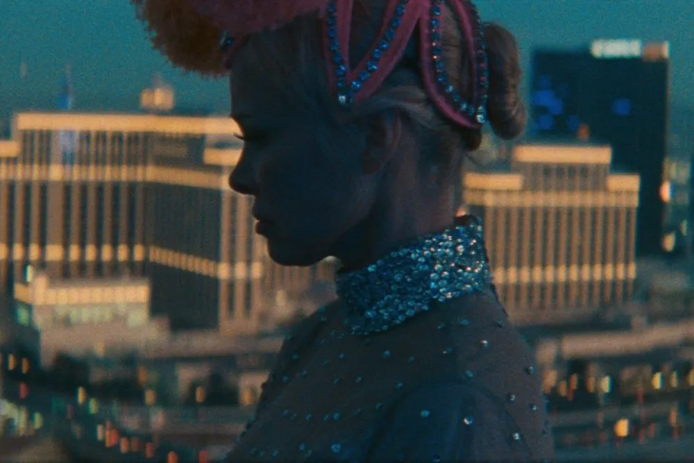 A woman in a sparkly showgirls' outfit viewed in profile next to a window.