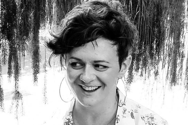 A black and white picture of a woman with short hair, looking to the side and smiling widely.