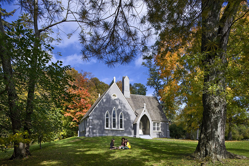 Three students sit in a circle on lawn outside a university building.