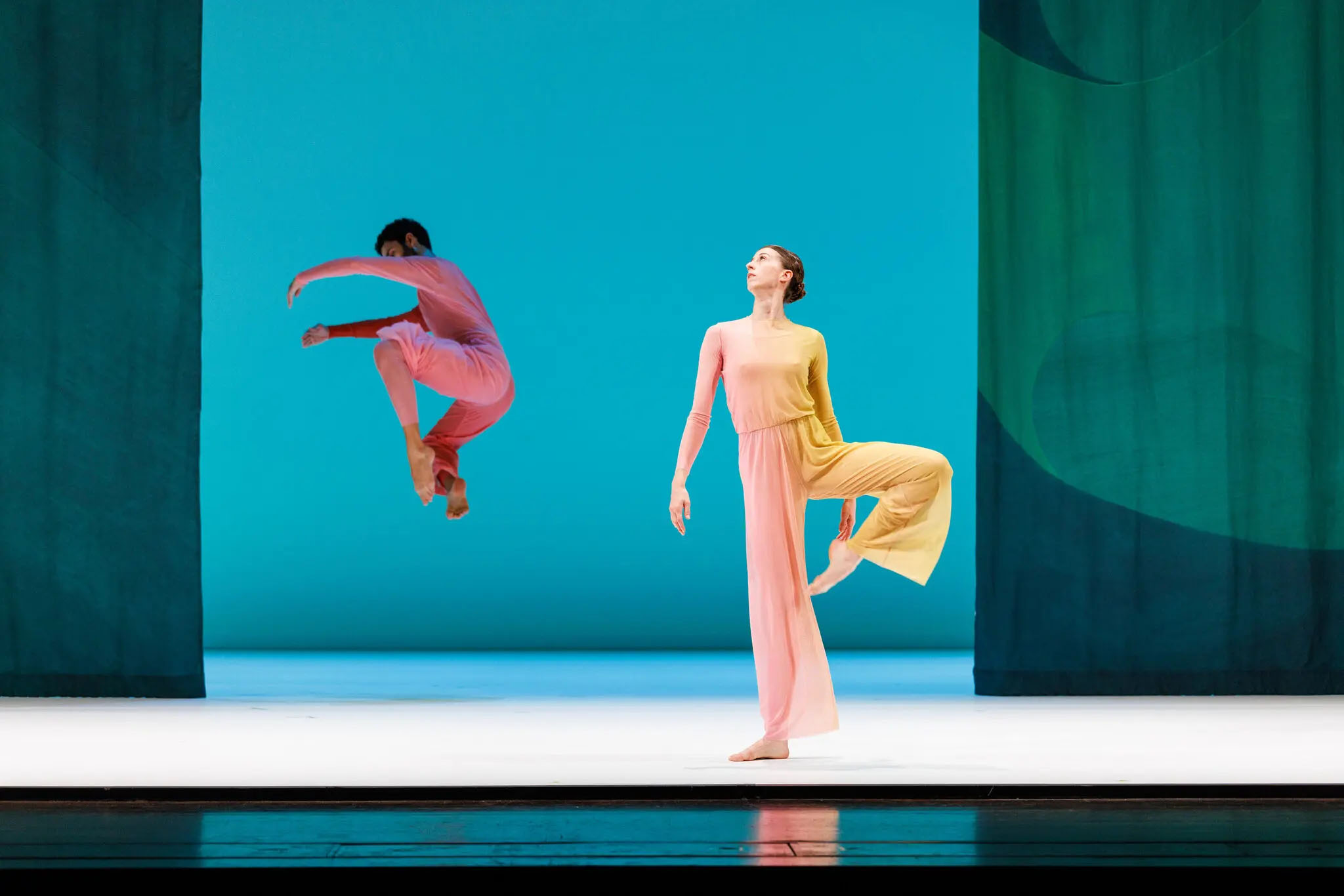 Two dancers in pastels move amidst a blue background