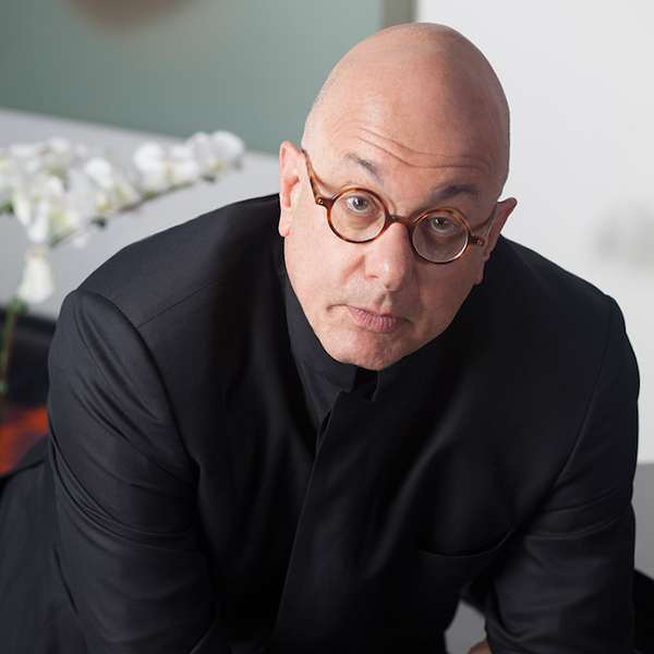 A man wearing black and in glasses looks at the camera. 