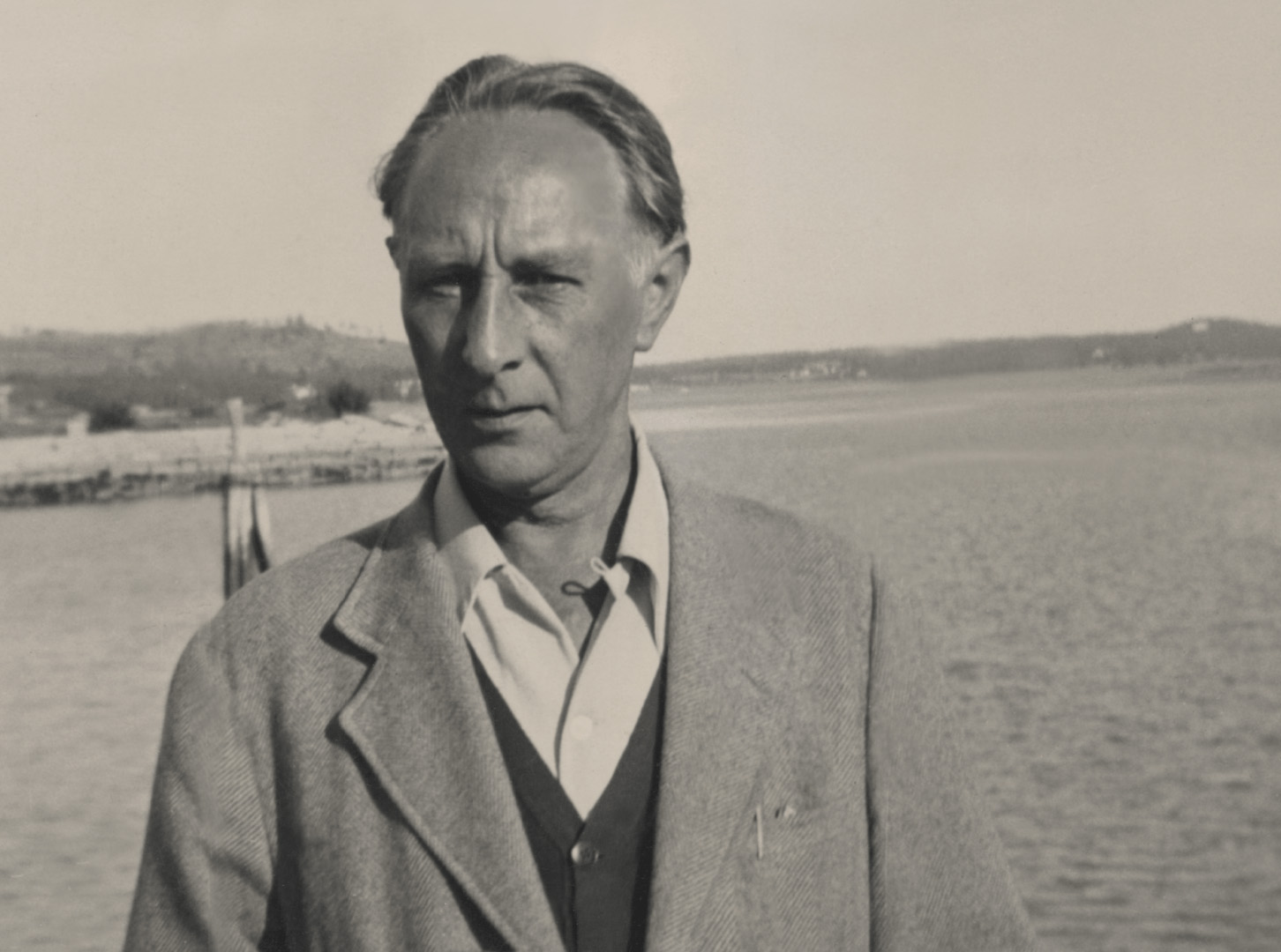 A black and white photo of a man with a dock and the sea behind him
