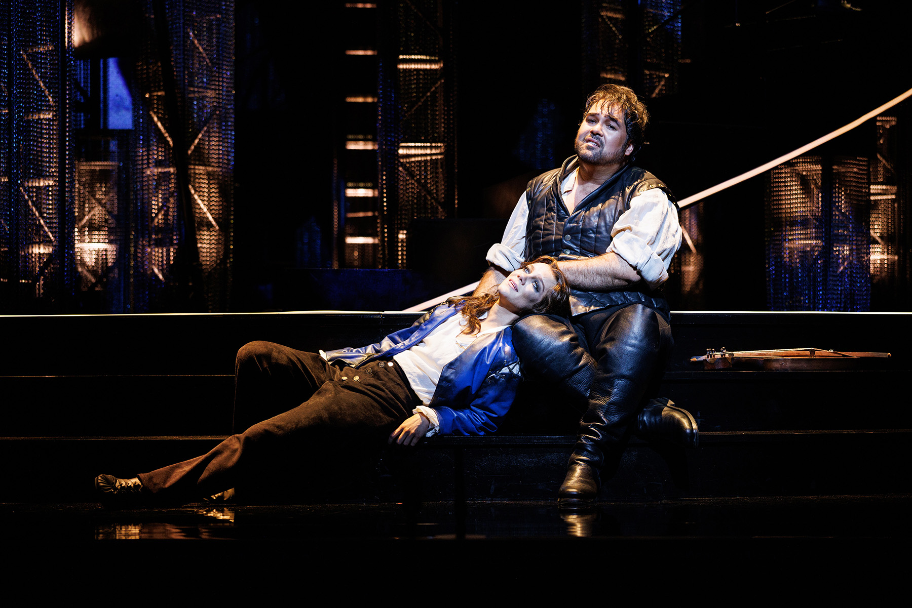A woman dressed in mistrel's clothing reclines against a man in a leather doublet on stage