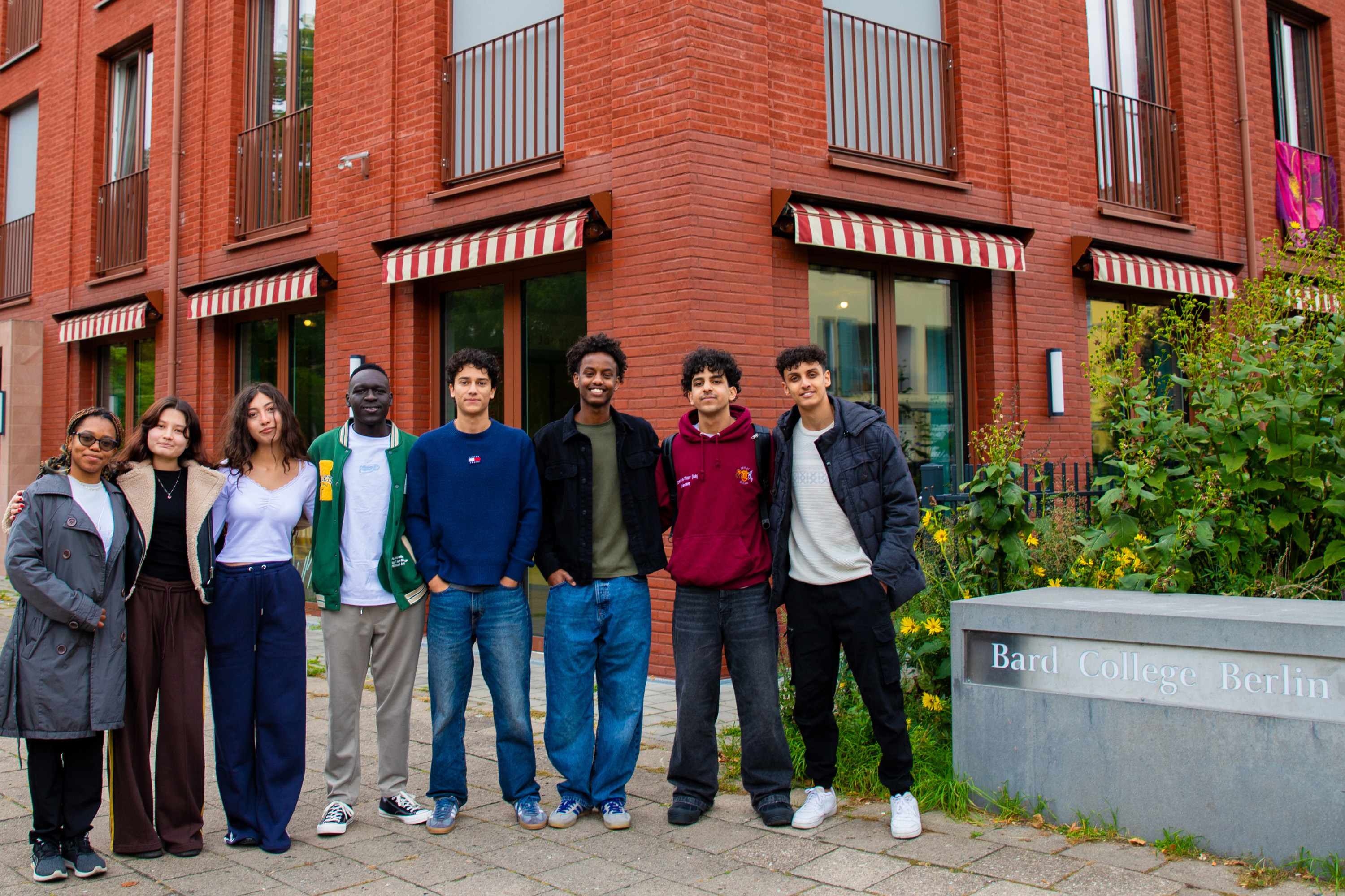 Eight students standing in a row next to a sign for Bard College Berlin.