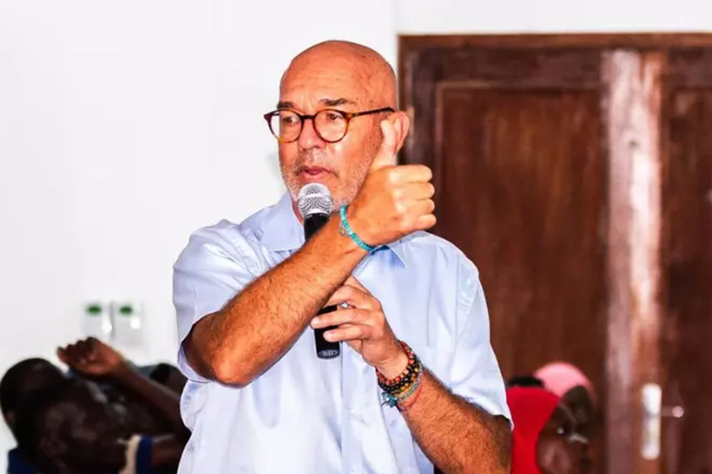 A man with a microphone speaks to a classroom full of attendees.