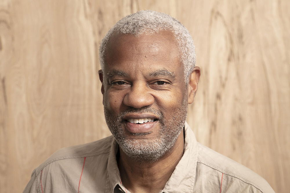 a man smiles at the viewer against a wood grained backdrop