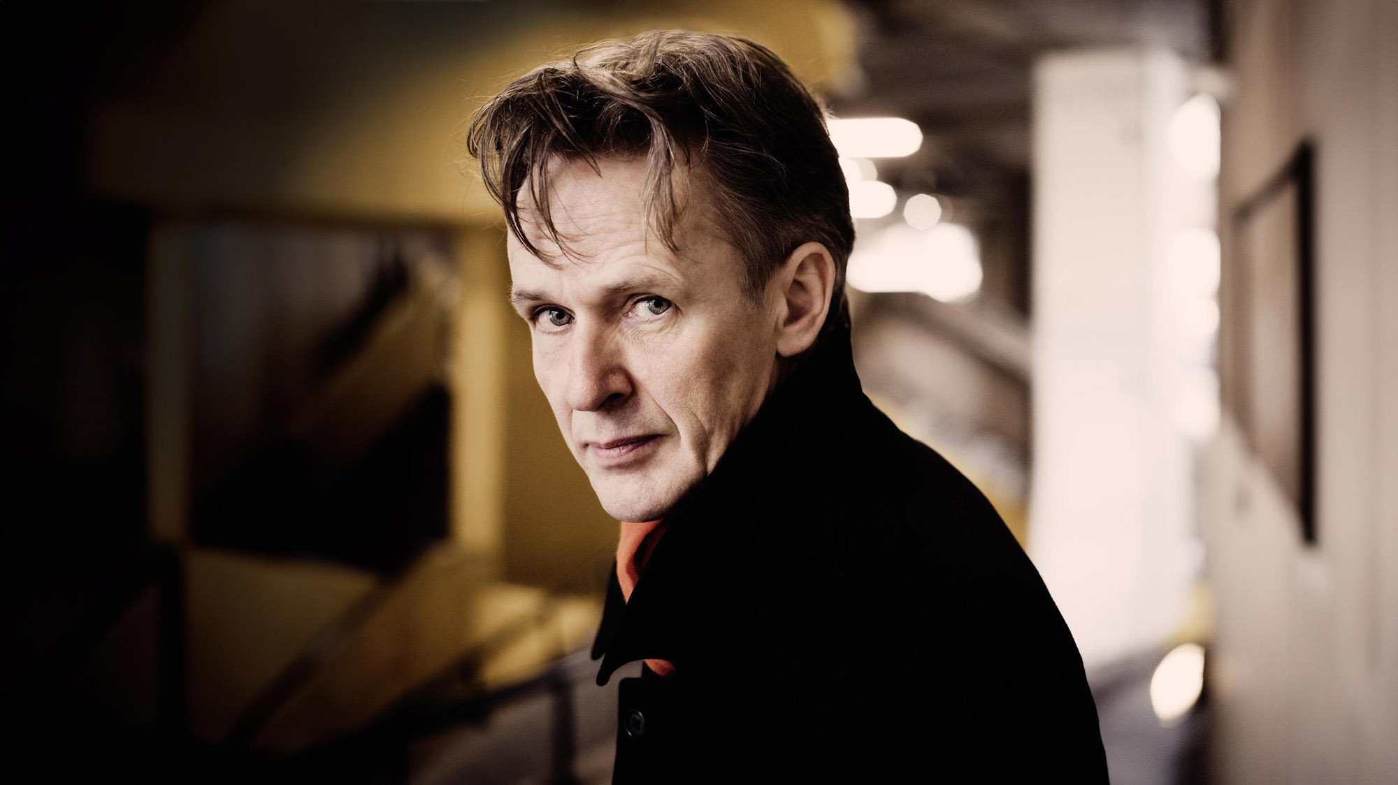 Ian Bostridge posing in a black coat for a portrait.