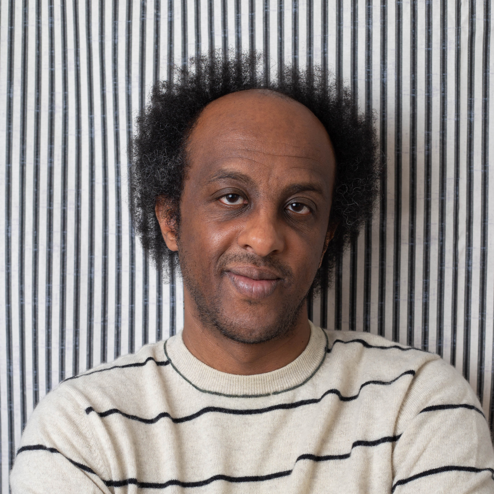 Professor Dinaw Mengestu smiling slightly for the camera.