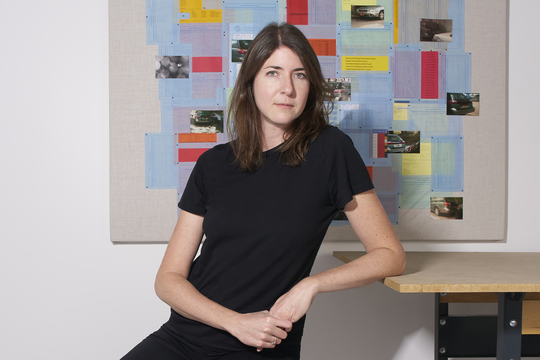 a woman in a black t-shirt sitting in a classroom gazes at the viewer