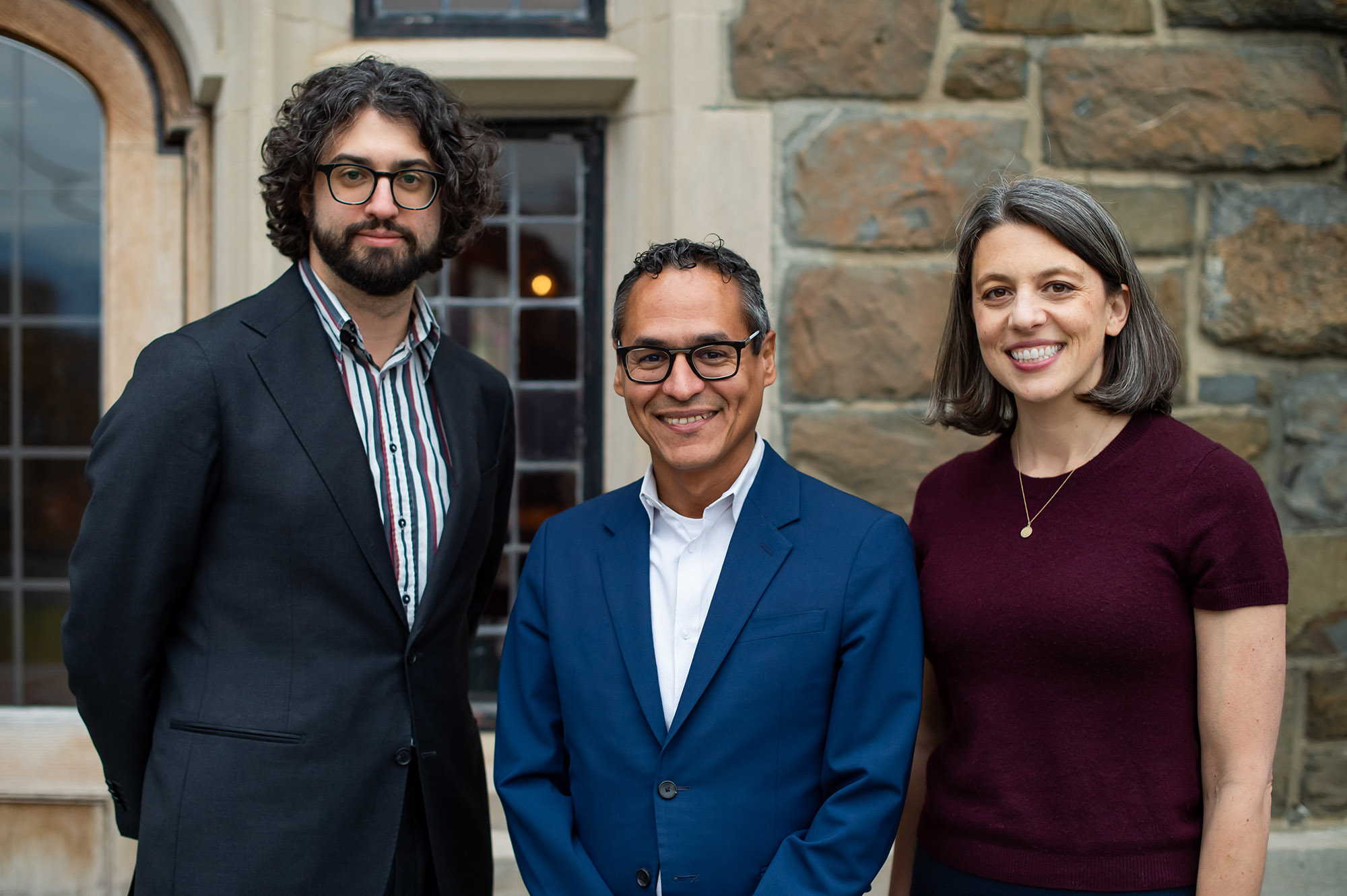 three people pose for a portrait in front of a stone building
