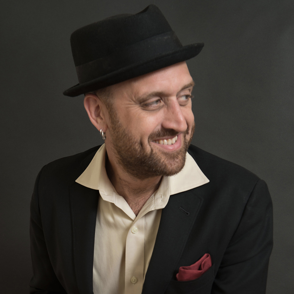 a man in a black hat and black jacket smiles as he looks to the side