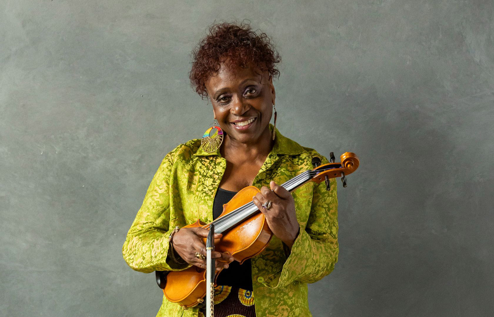 a woman in a yellow jacket holds the violin