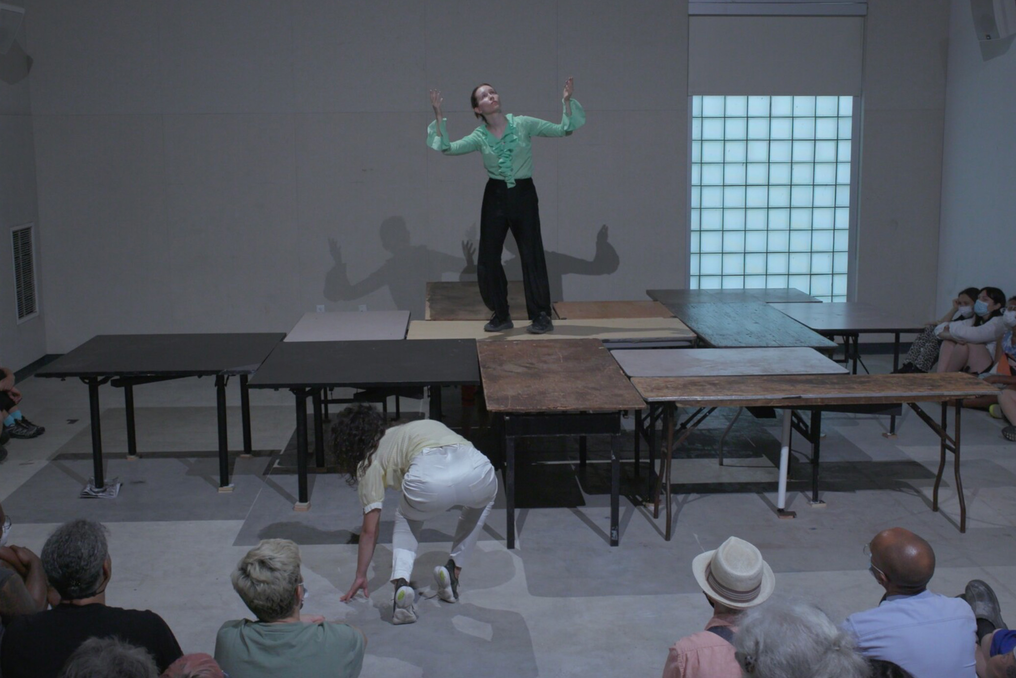 A person in a button up shirt with their hands up standing on a table, in a dance performance.