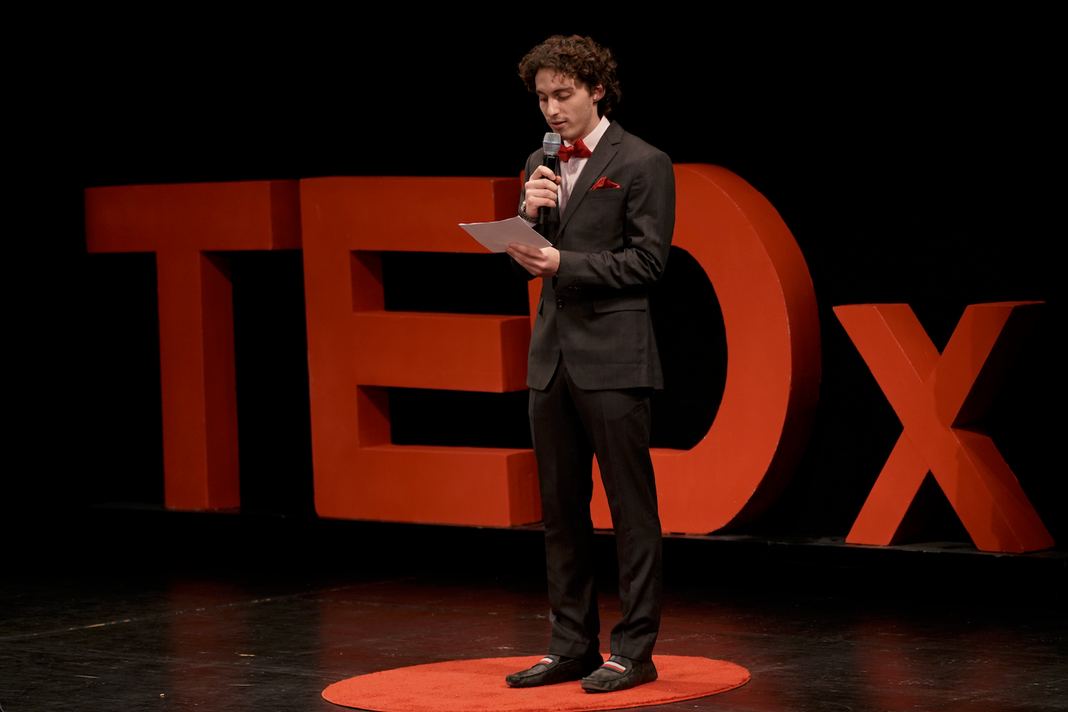 A presenter stands in front of the Tedx logo.