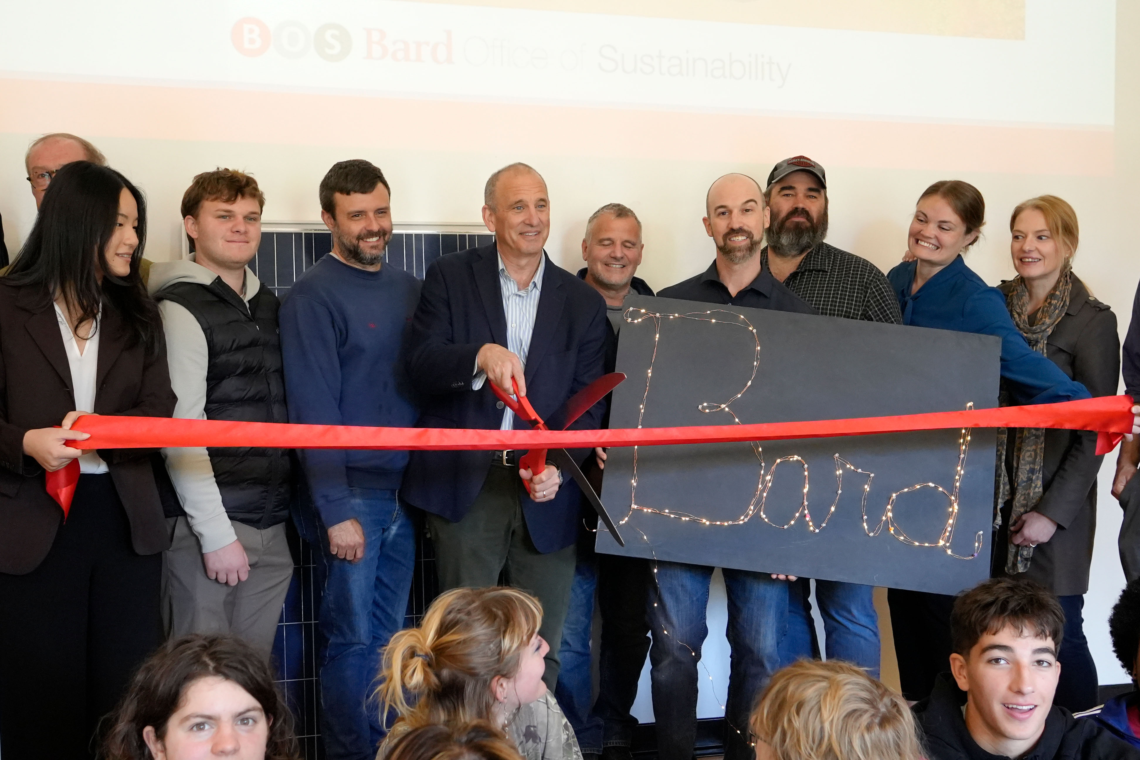 A group of people cutting a large red ribbon with scissors in celebration.