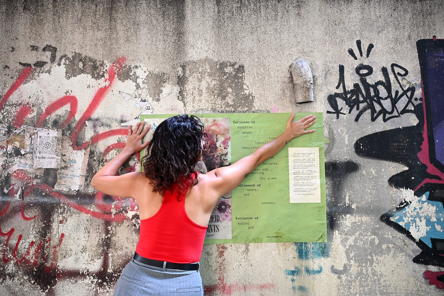 Woman putting up poster on a cement wall coverd in graffiti.
